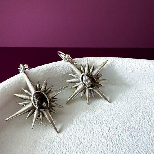 Pair of star-shaped earrings on a white surface with a purple background