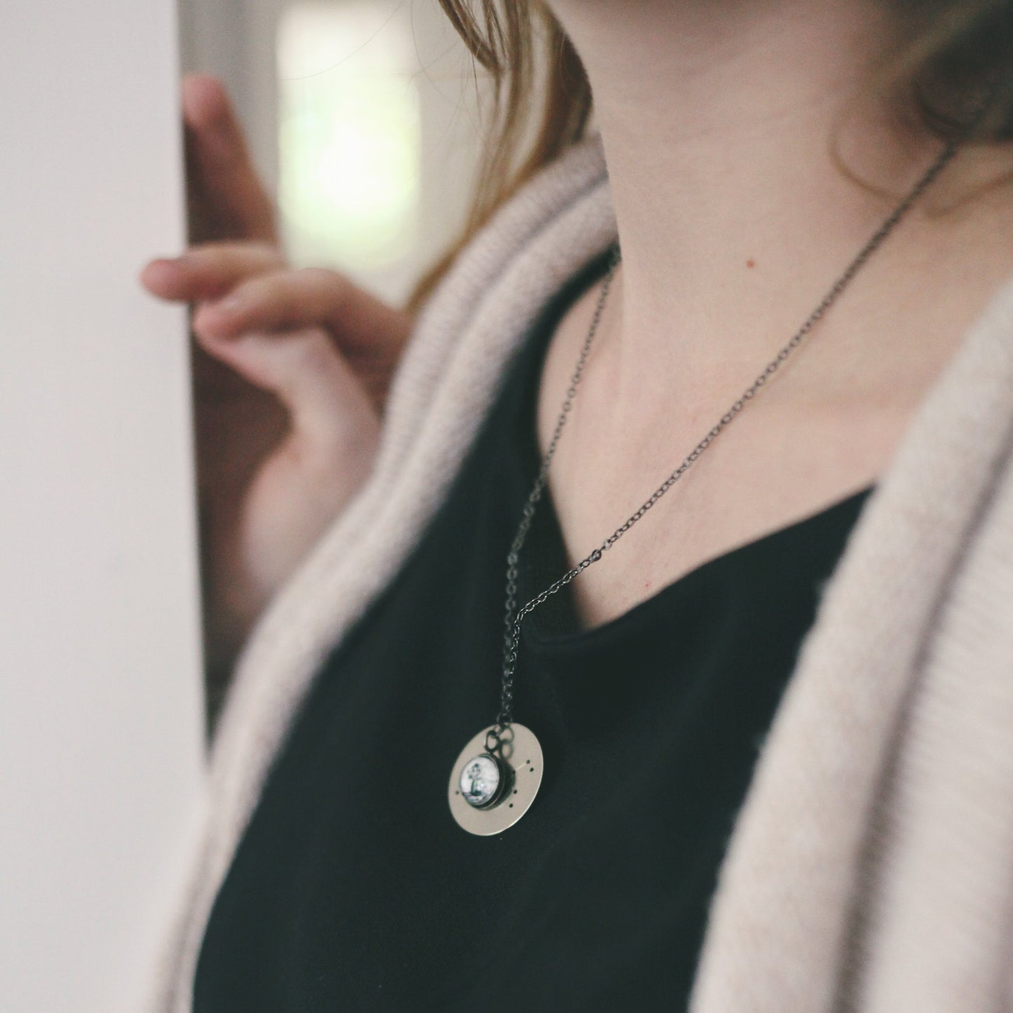 Woman in a sweater wearing a silver constellation necklace standing at an angle leaning in a doorframe.