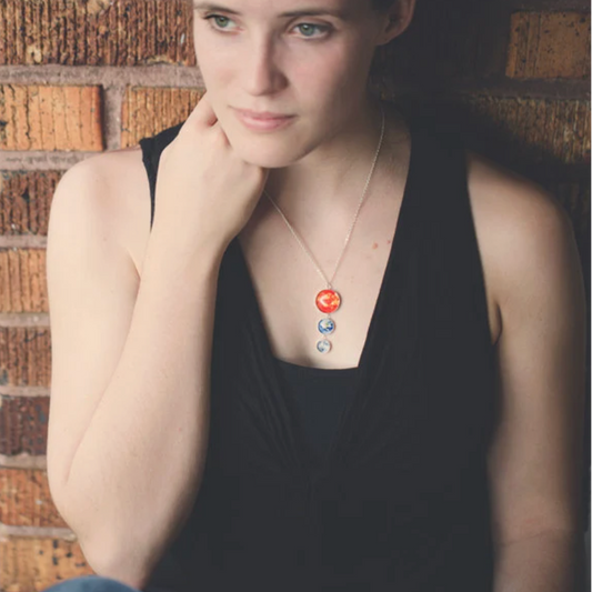 Women wearing sun, earth and moon necklace leaning against a brown brick wall.