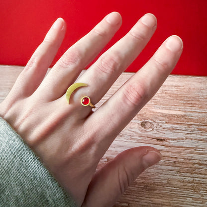 Hand wearing a ring with a birthstone on a wooden surface and red background