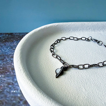 Black chain bracelet with a uranus charm on a white surface with a blue background
