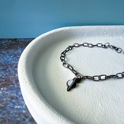 Black chain bracelet with a uranus charm on a white surface with a blue background