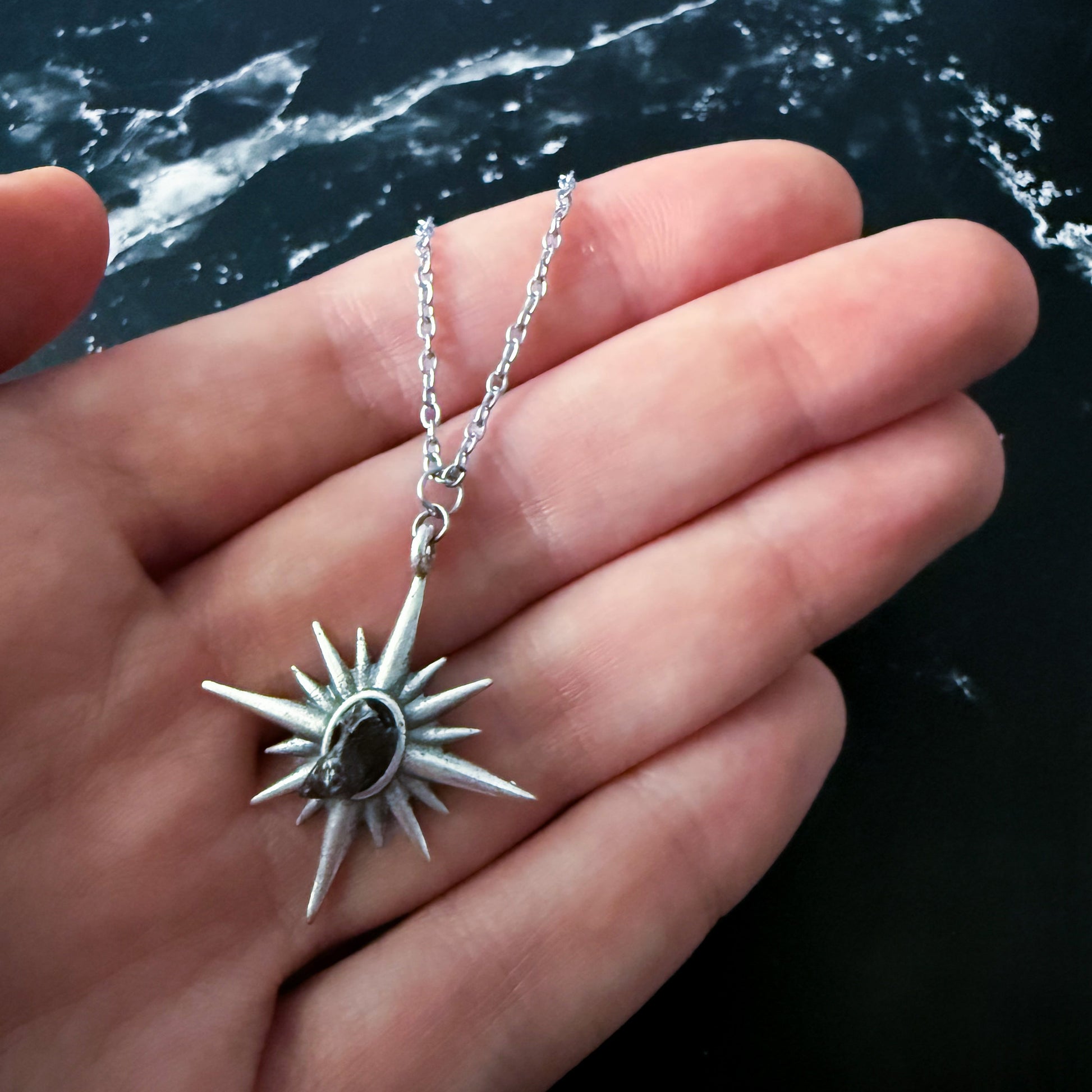 Supernova Starburst Necklace with Authentic Meteorite held in a hand against a dark marble background