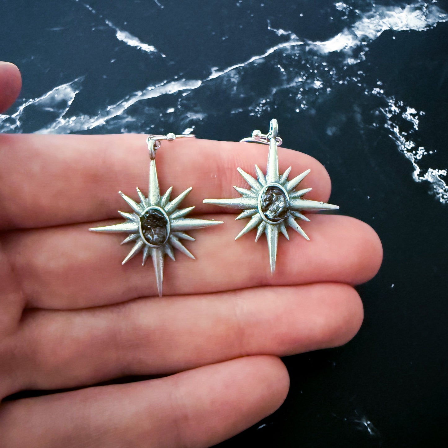 Silver star-shaped earrings held in a hand with a dark background