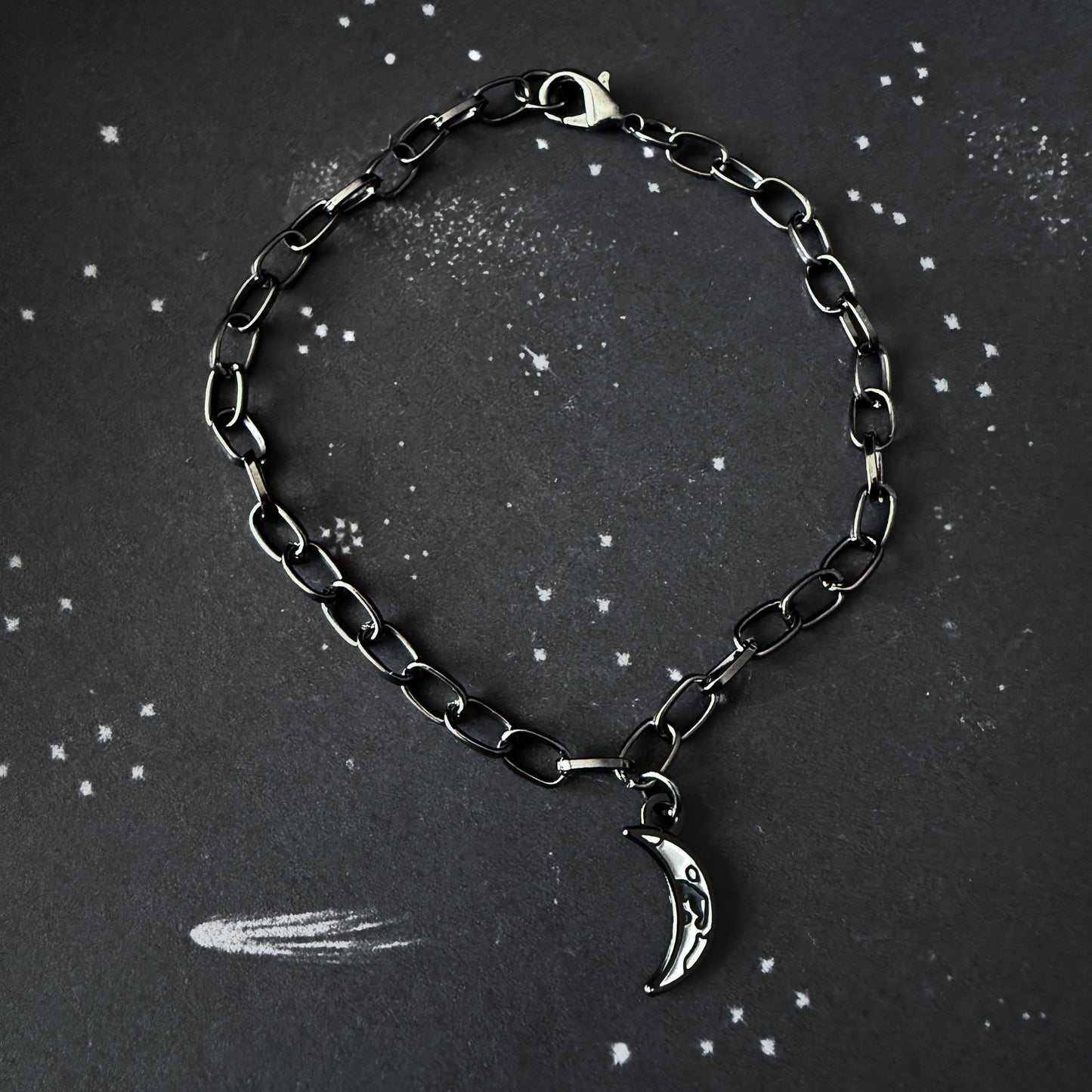 Black chain bracelet with a silver moon charm on a dark background