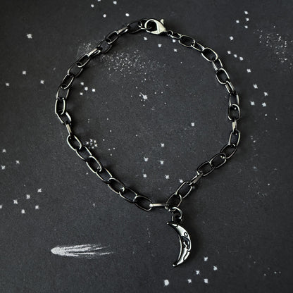 Black chain bracelet with a silver moon charm on a dark background