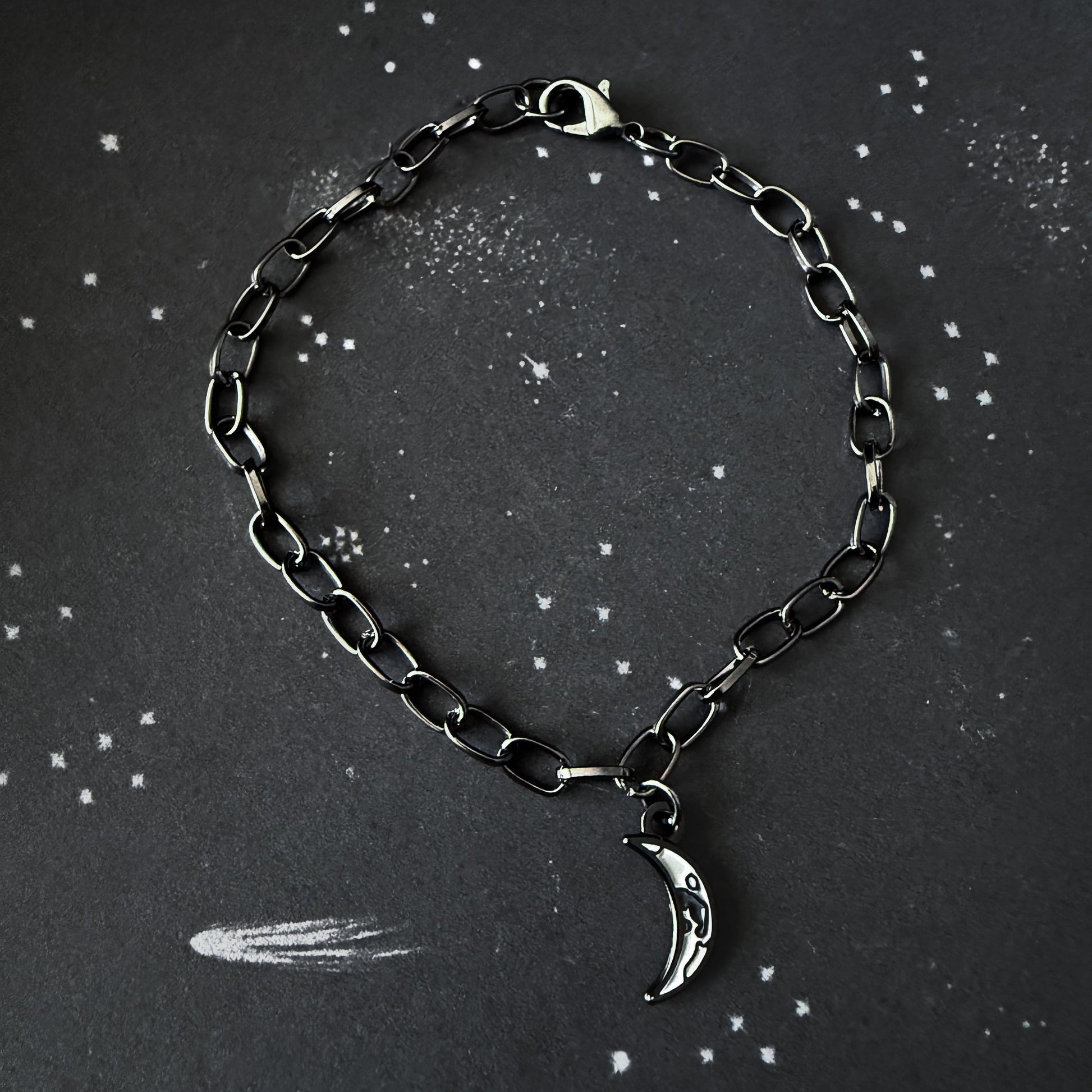 Black chain bracelet with a silver moon charm on a dark background
