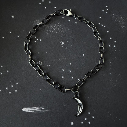 Black chain bracelet with a silver moon charm on a dark background