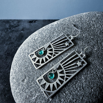 Pair of silver earrings with birthstones on a textured stone surface