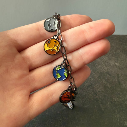 Hand holding a charm bracelet with four planet charms against a neutral background