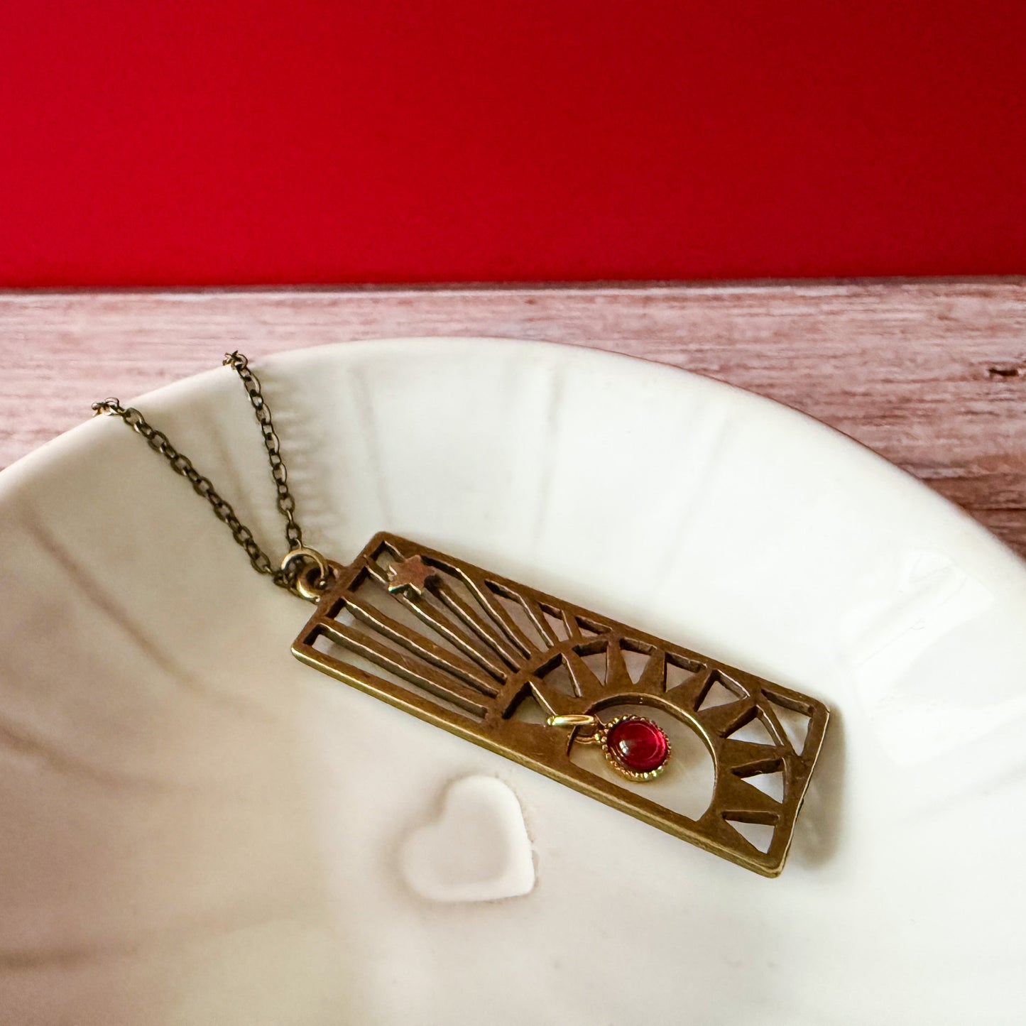 Brass pendant with a birthstone on a white dish with a red background