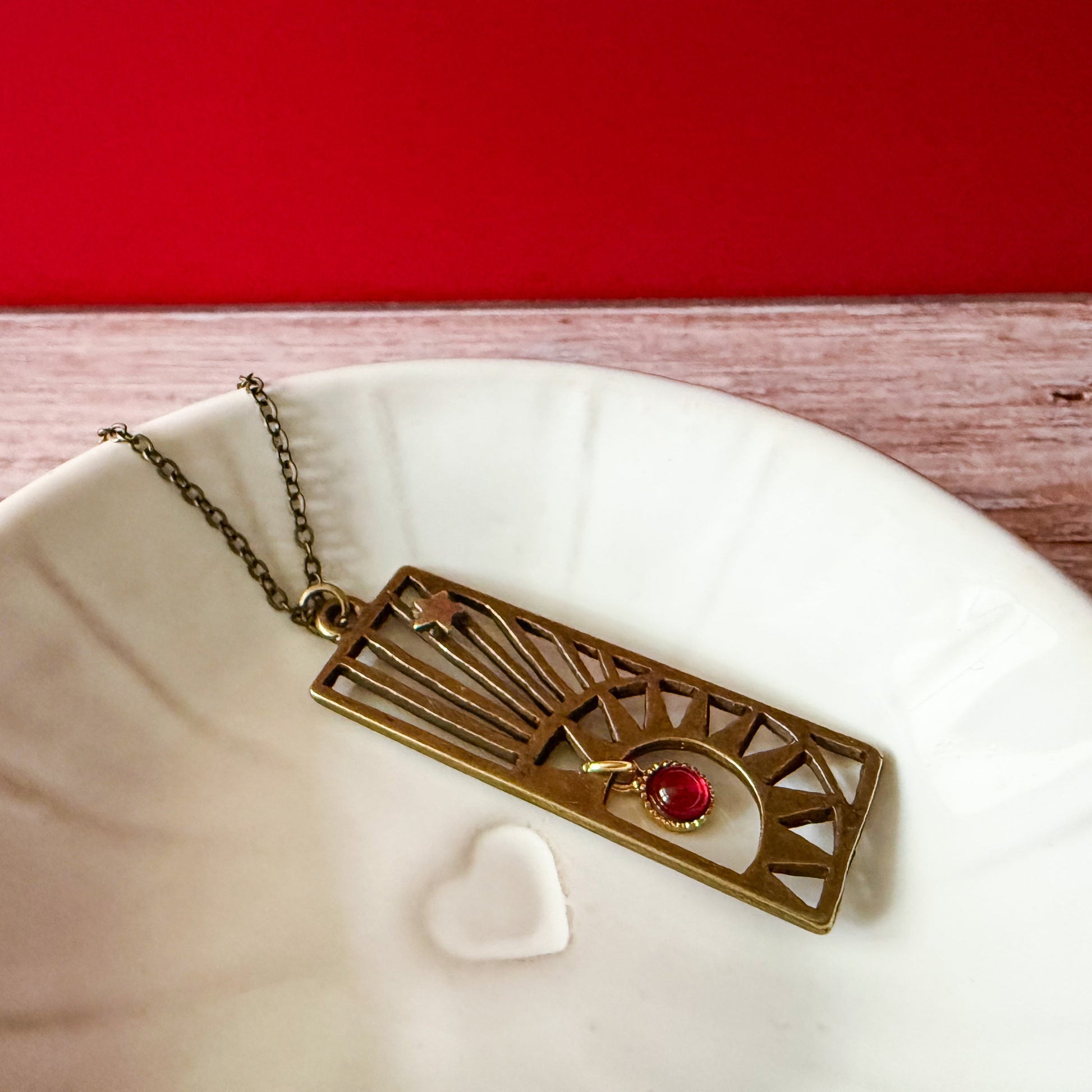 Brass pendant with a birthstone on a white dish with a red background