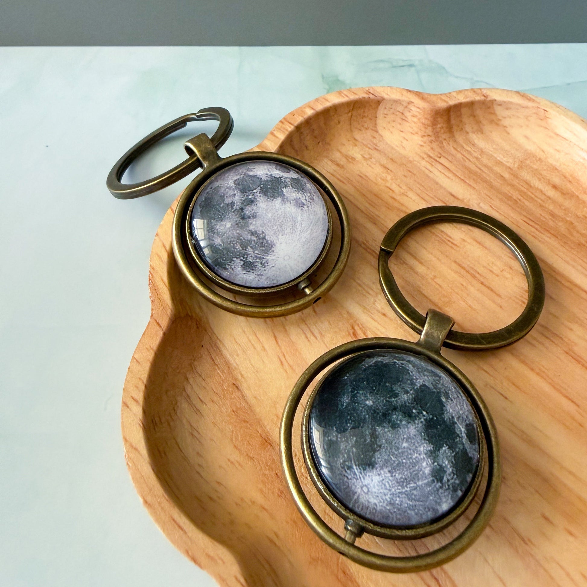 Two moon-themed keychains on a wooden surface with a light background