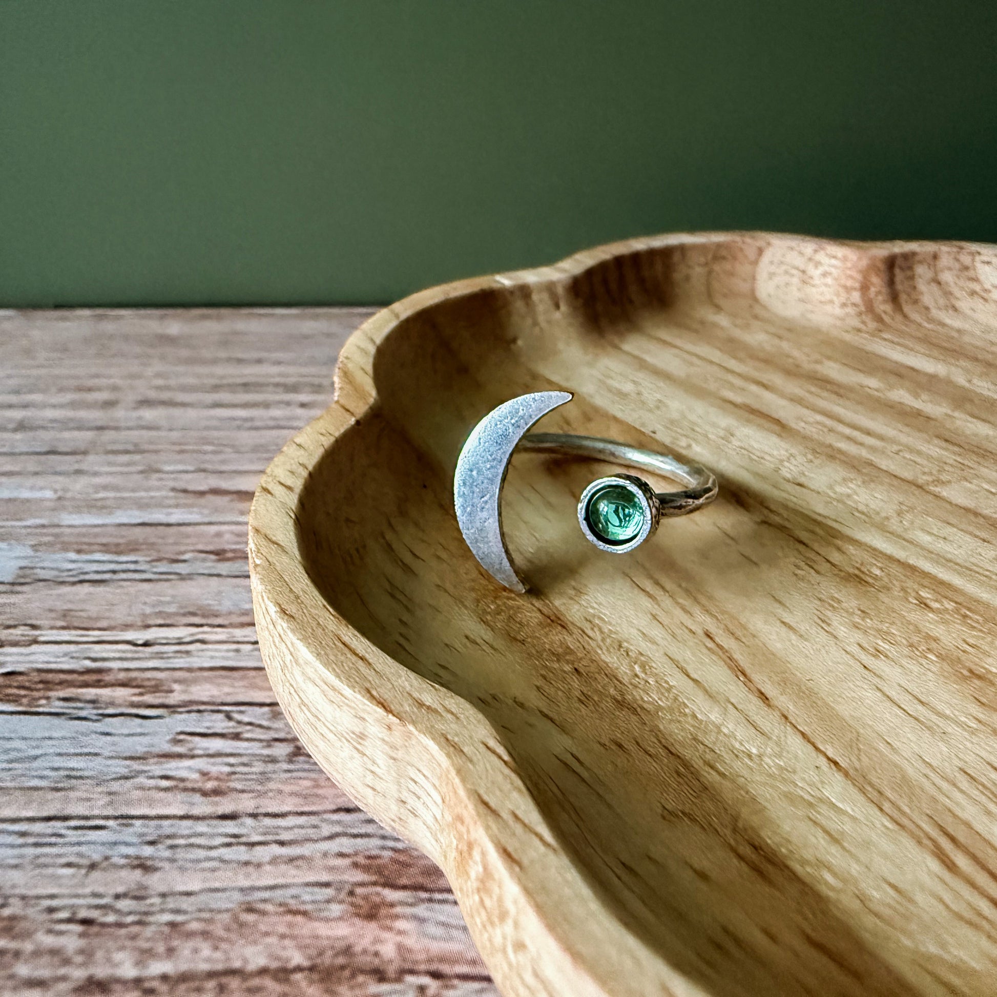 Silver crescent moon ring on a wooden surface with a green background.