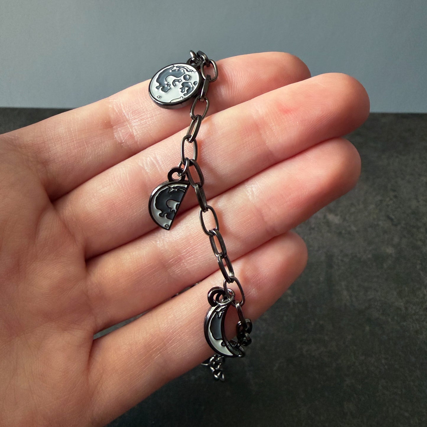 Hand holding a small chain with moon charms against a neutral background