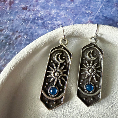 Silver earrings with sun and moon designs on a textured surface