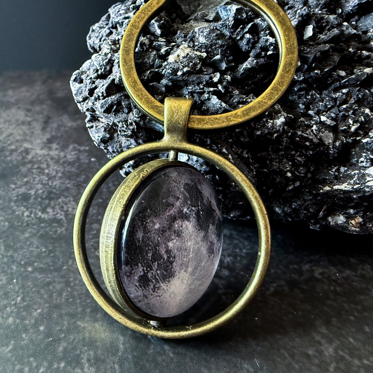 Bronze Keychain leaning on a dark textured rock.
