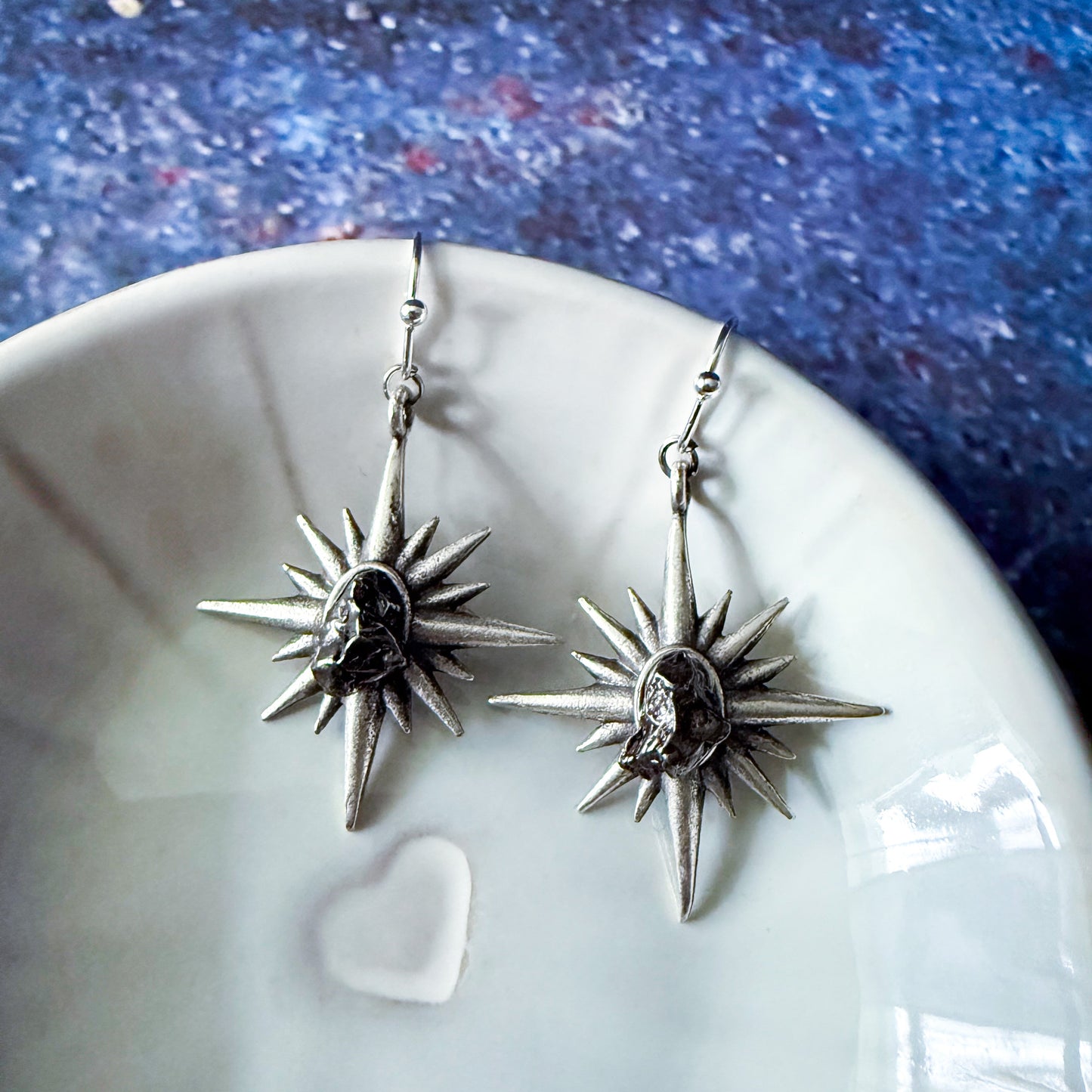 Silver star-shaped earrings on a white dish with a blue textured background