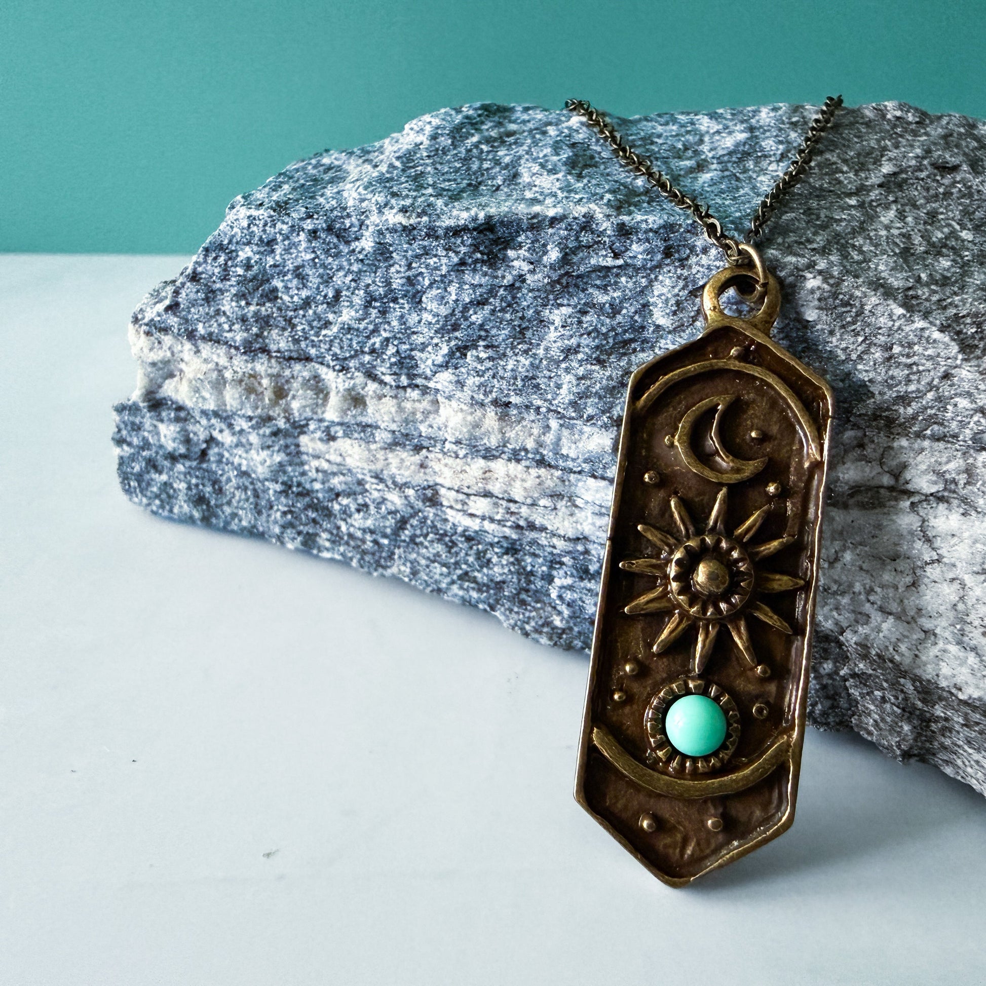 Bronze pendant necklace with turquoise stone on a rock