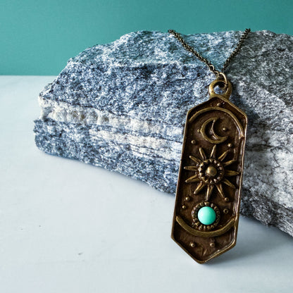 Bronze pendant necklace with turquoise stone on a rock
