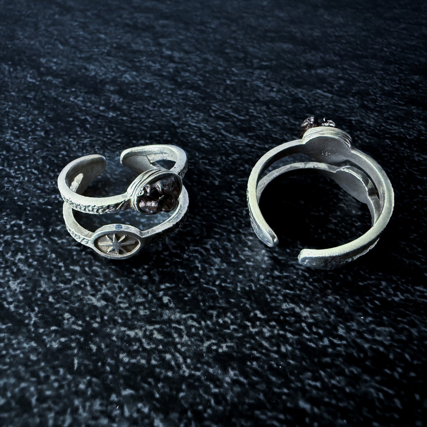 Two silver rings with meteorite fragments on a dark textured surface