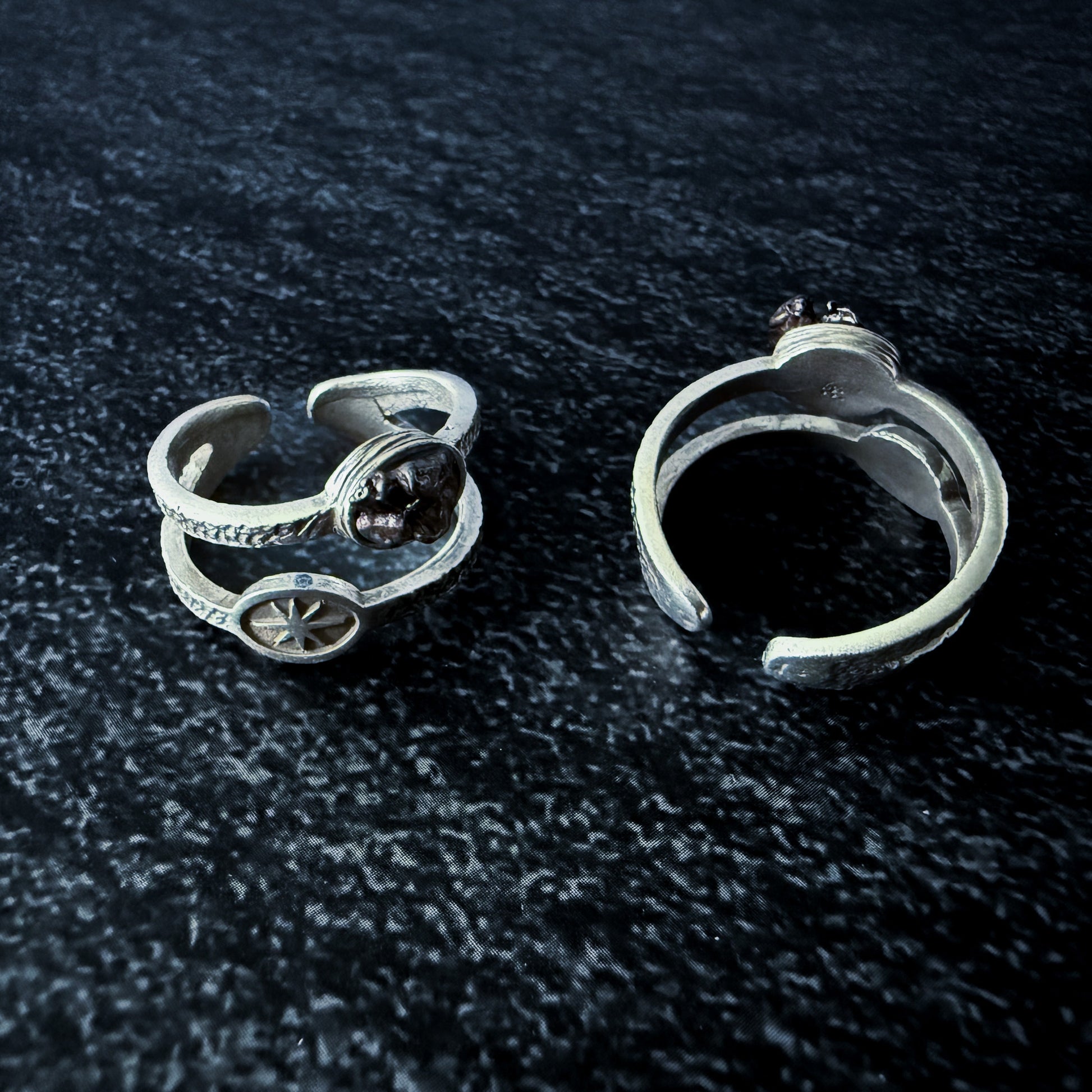 Two silver rings with meteorite fragments on a dark textured surface