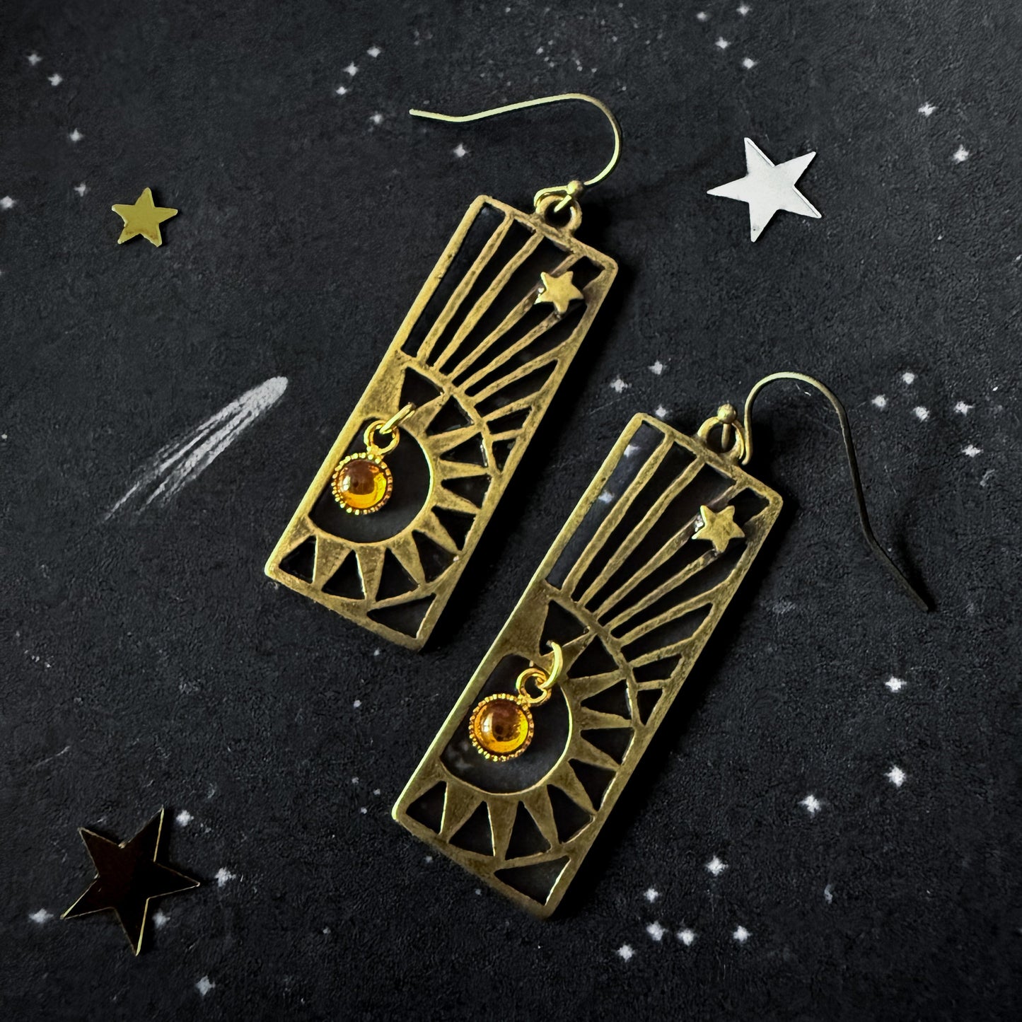 Pair of bronze earrings with star designs on a dark background