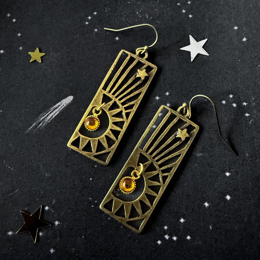 Pair of bronze earrings with star designs on a dark background