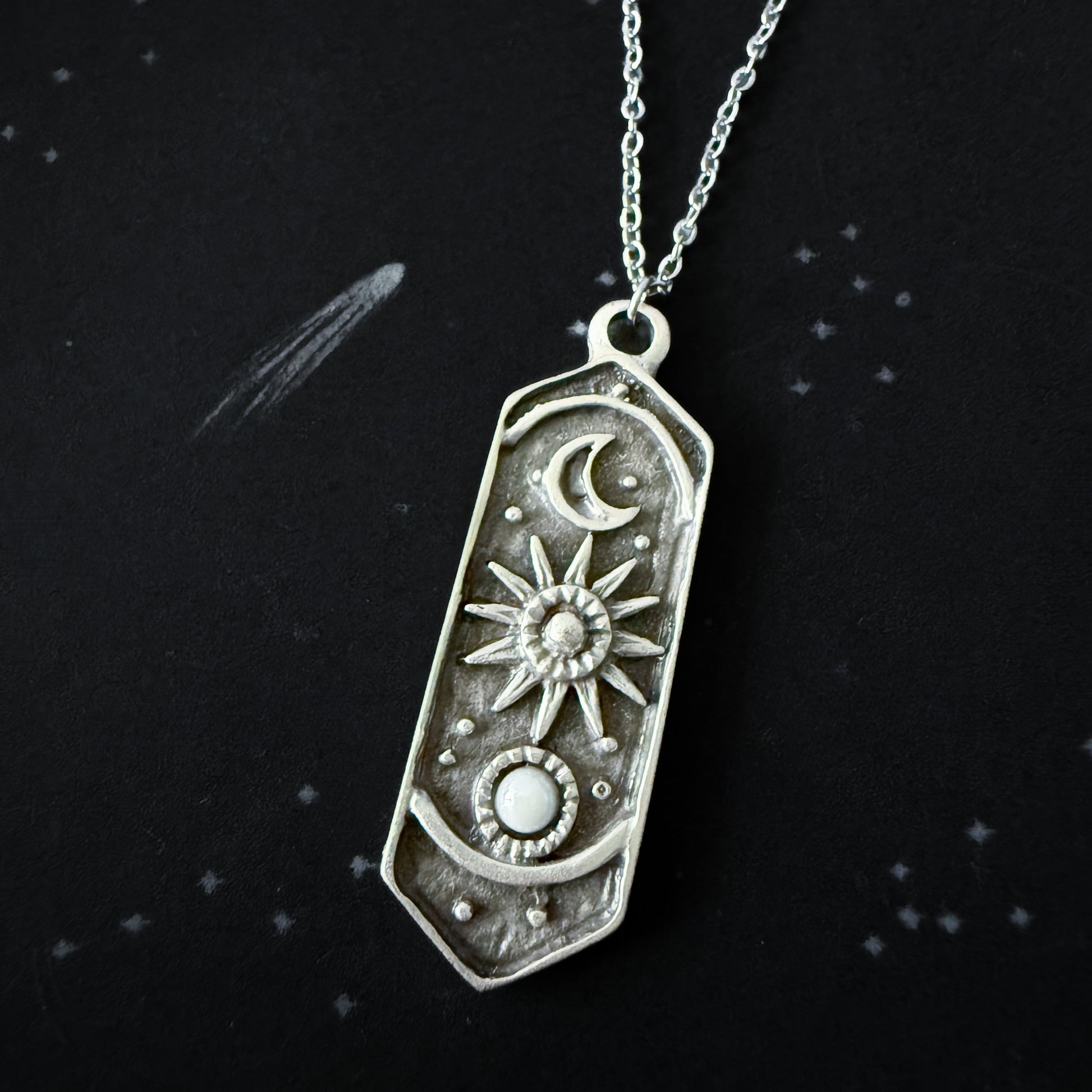 Silver pendant necklace with celestial design on a black background
