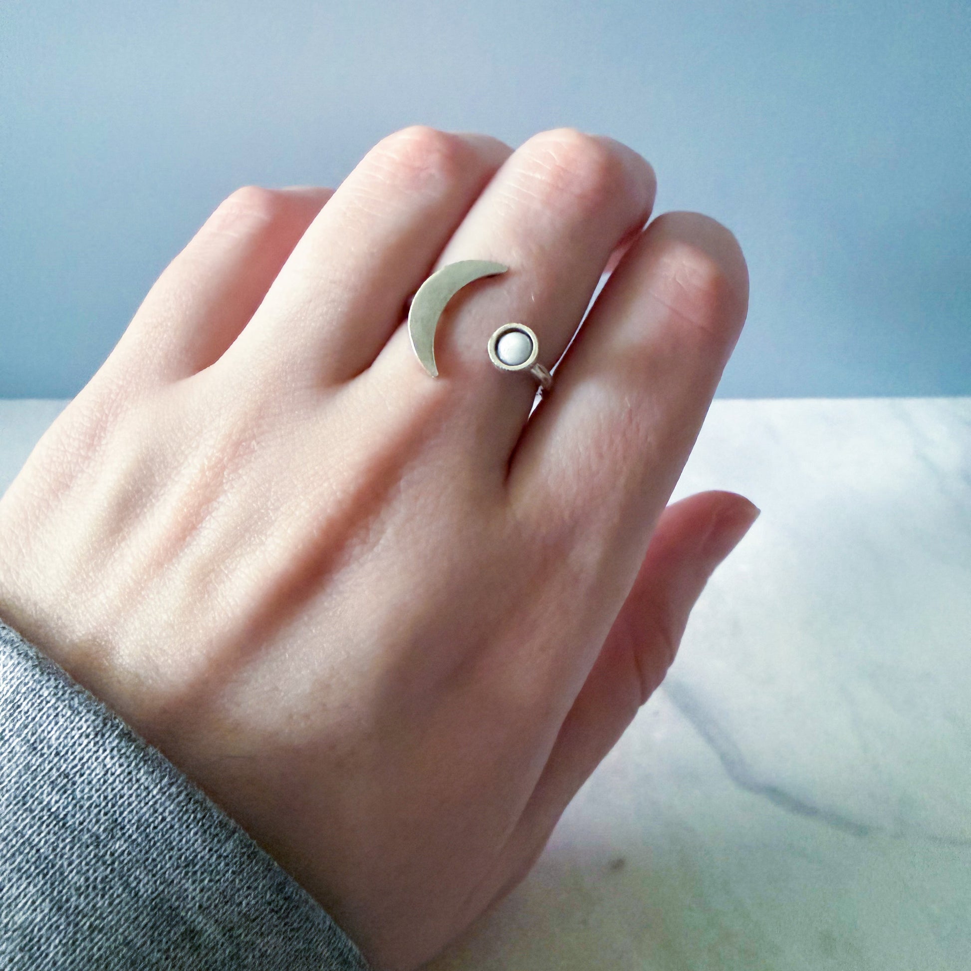 Hand wearing a ring with a moon design on a light blue background