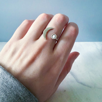 Hand wearing a ring with a moon design on a light blue background