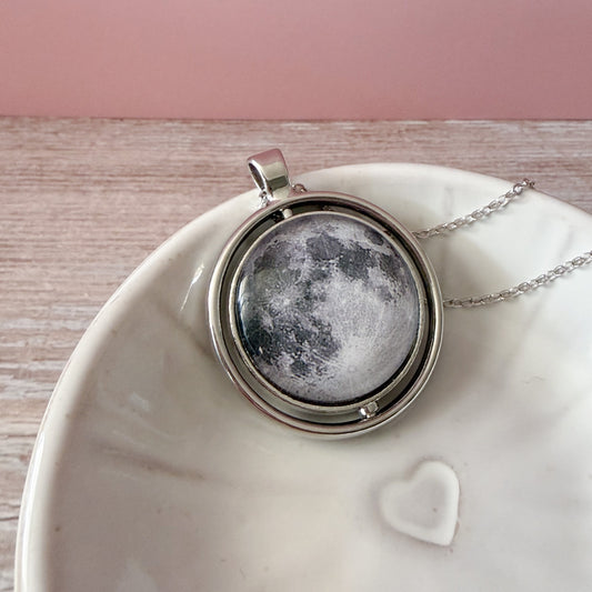 Moon-phase necklace on a white dish with a pink background