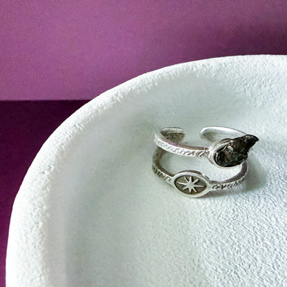Silver ring with star design on a white stand against a purple background