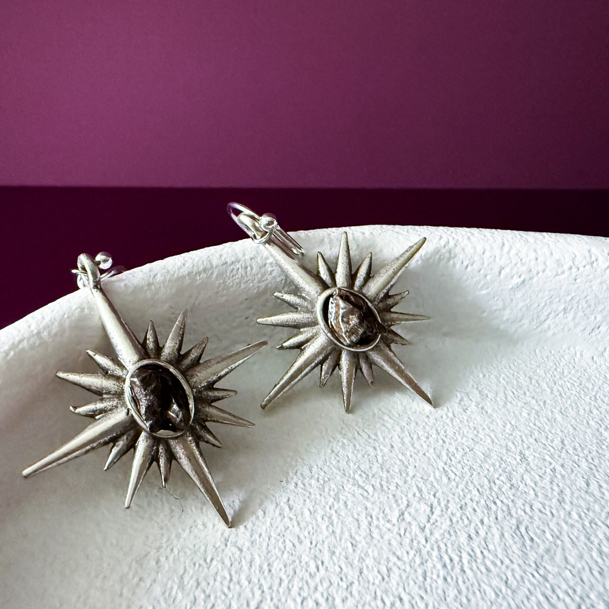 Pair of star-shaped earrings on a white surface with a purple background