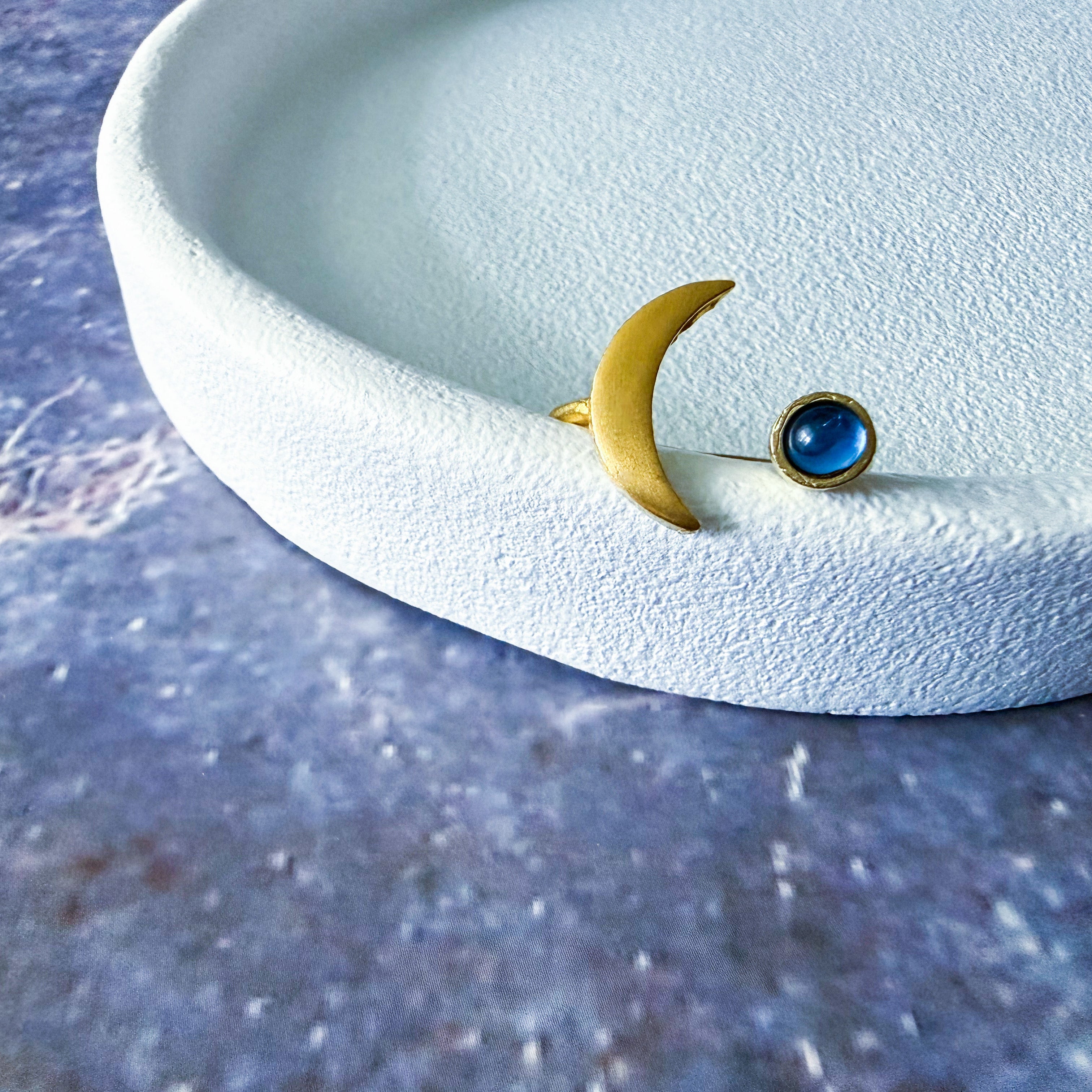 Gold crescent moon ring with birthstone on a white dish