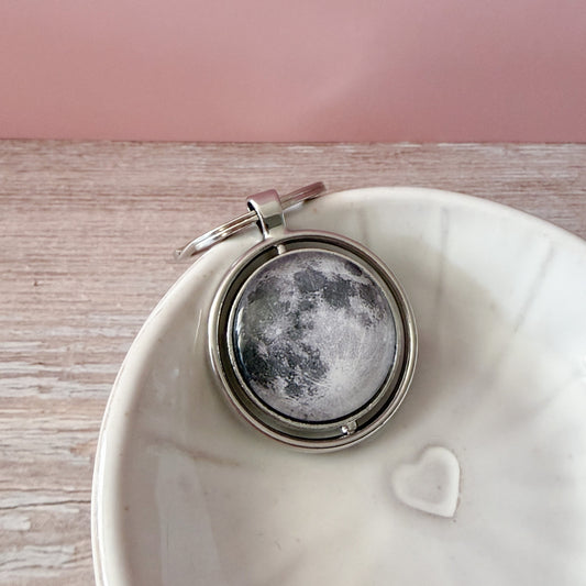 Keychain with moon design on a white dish against a pink background