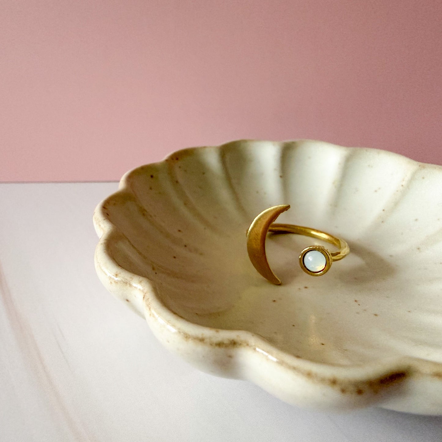 Shell-shaped trinket dish with a gold ring and birthstone on a pink background