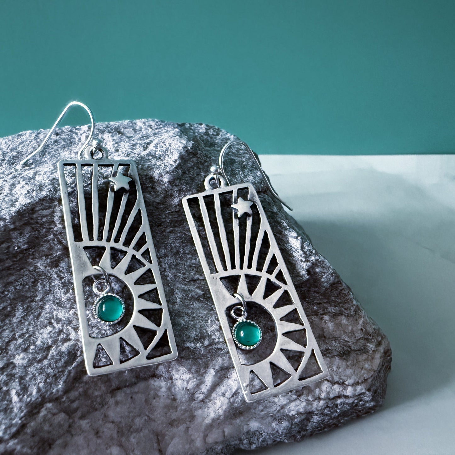 Silver earrings with birthstones on a rock against a teal and white background