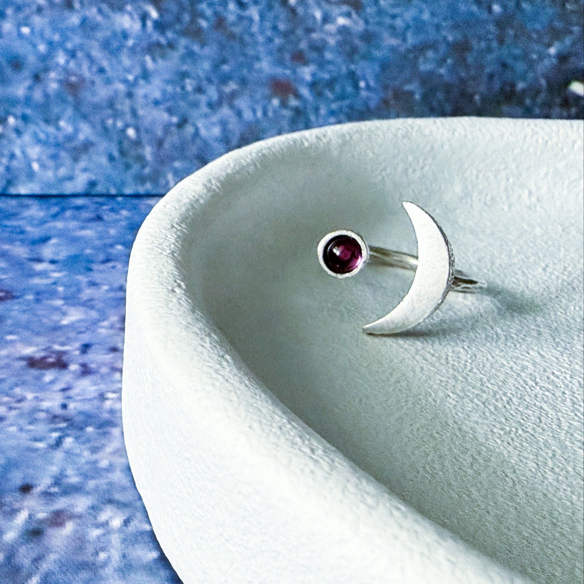 Silver ring with a birthstone on a textured blue surface
