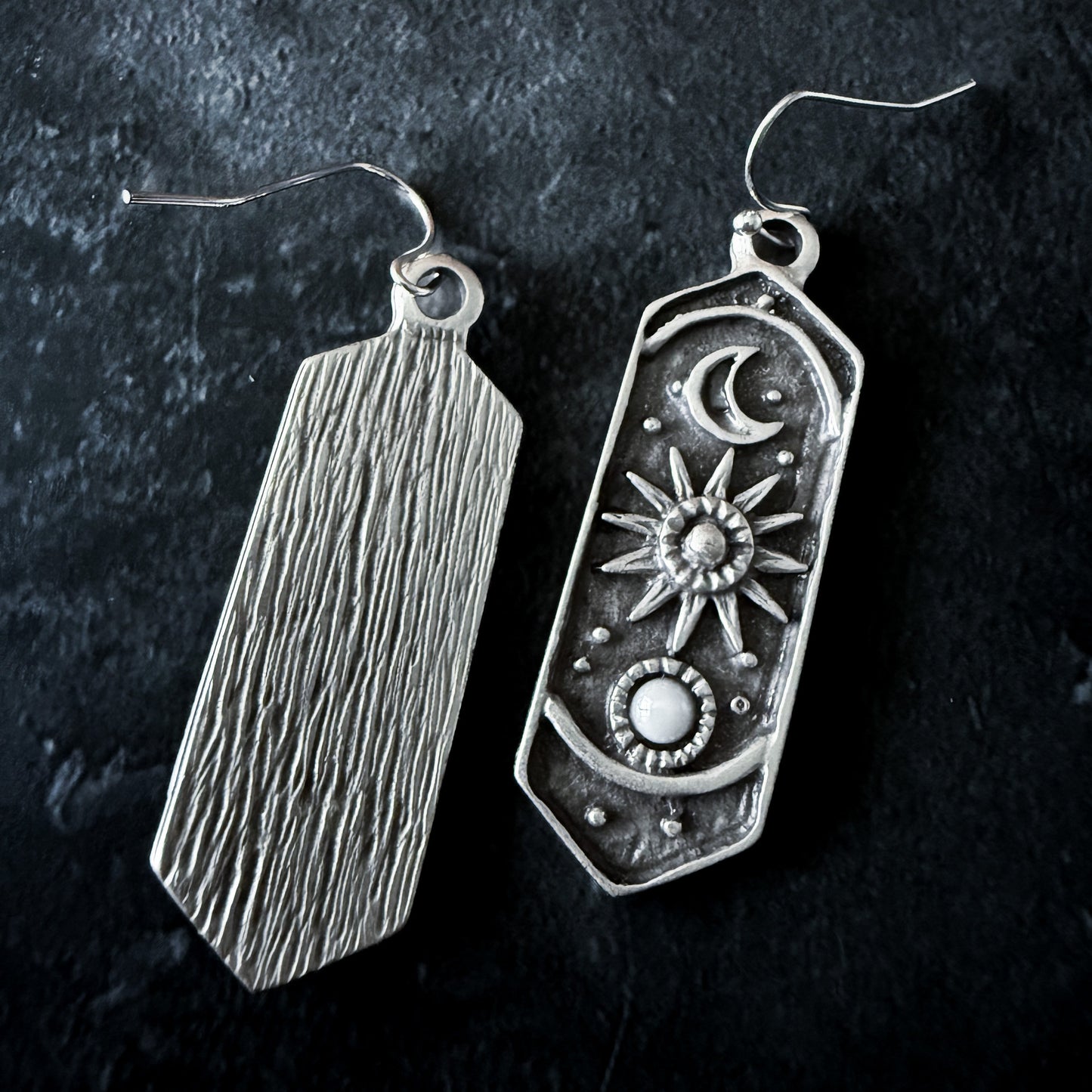 Two silver earrings on a dark background