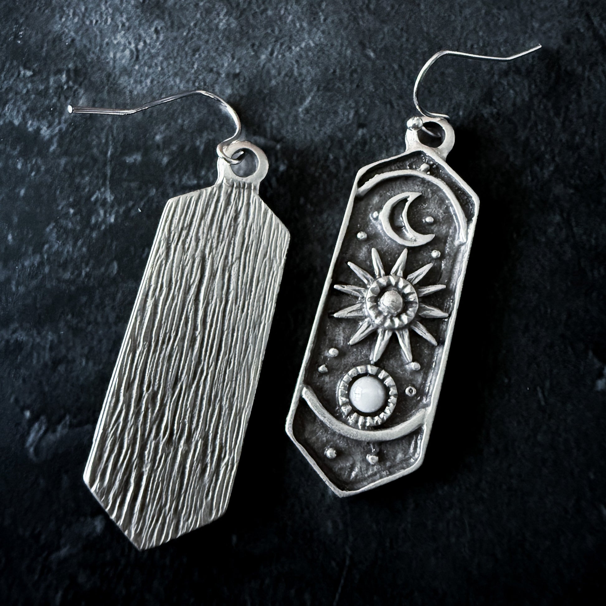 Two silver earrings on a dark background