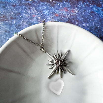 Silver star-shaped pendant necklace on a white dish with a blue textured background