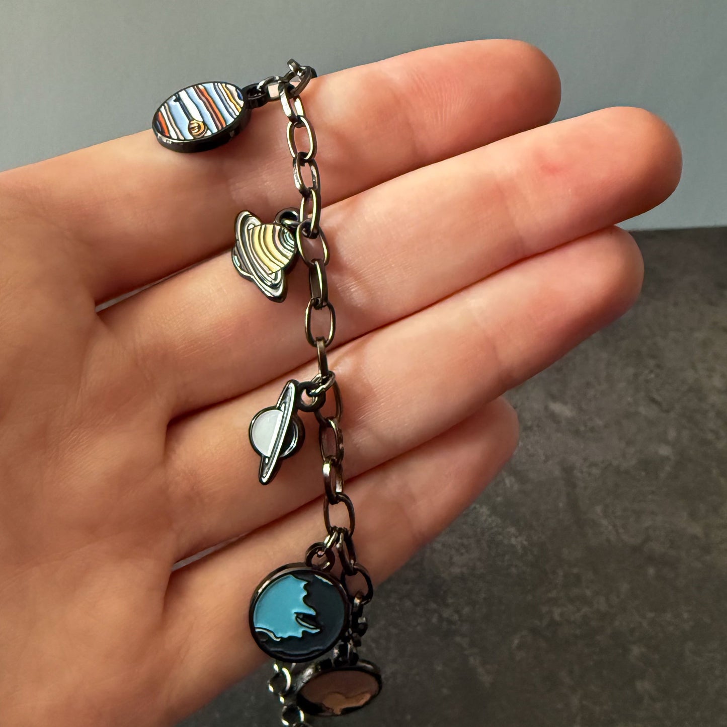 Hand holding a bracelet with various charms against a neutral background