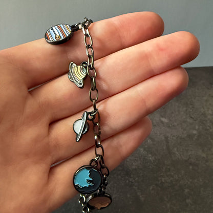 Hand holding a bracelet with various charms against a neutral background