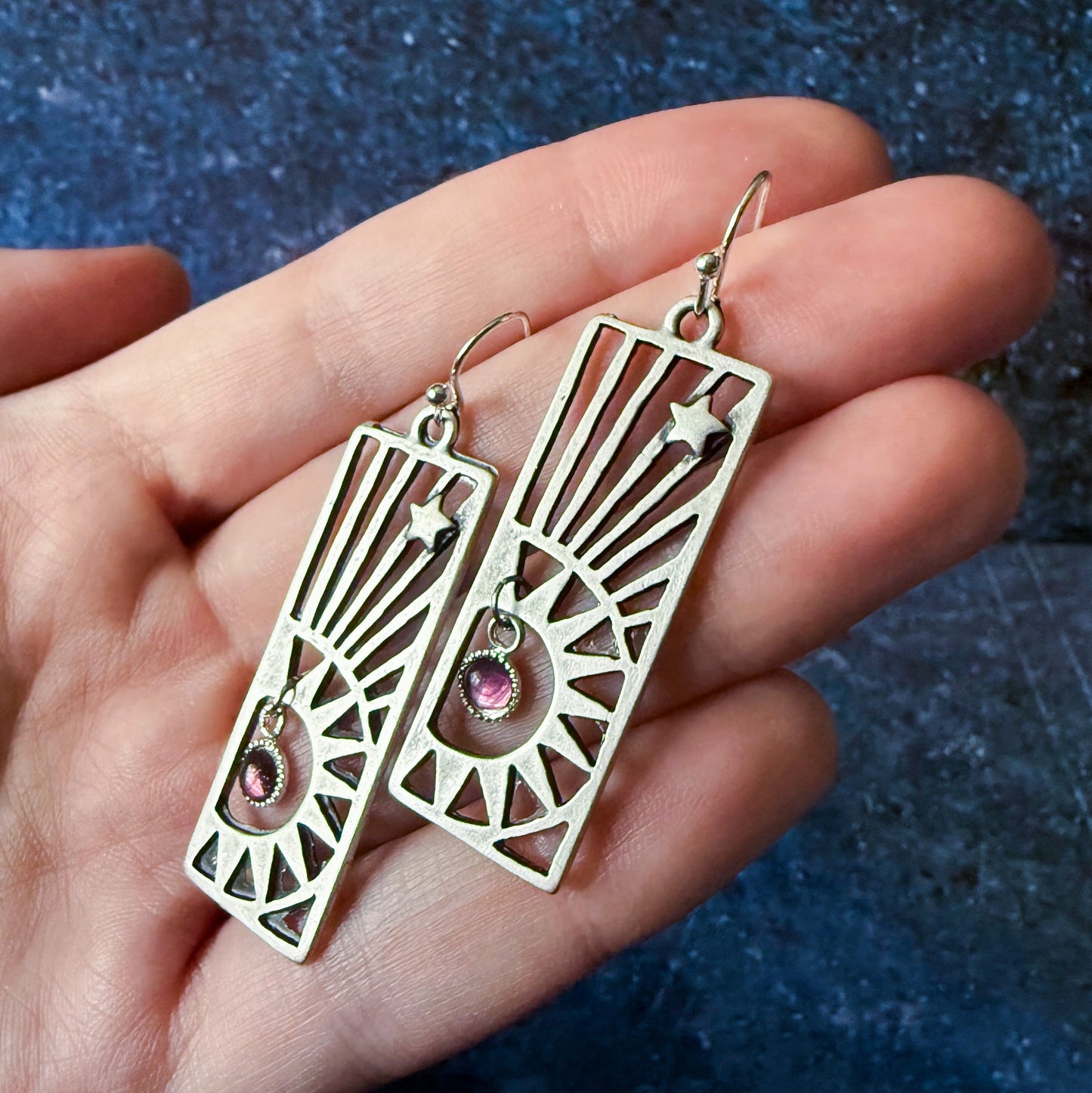 Decorative earrings held in a hand against a blue textured background