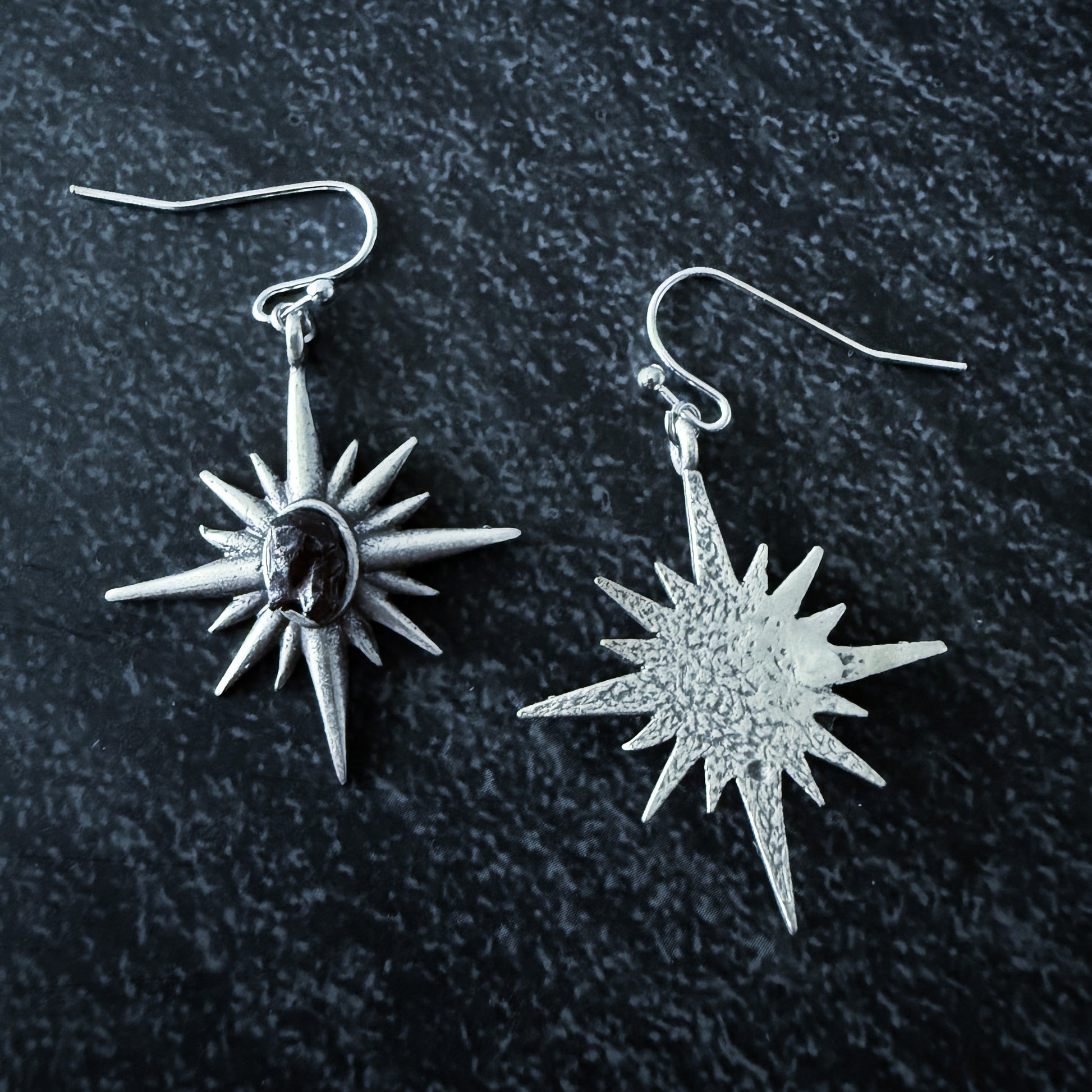 Star-shaped silver earrings on a dark textured background