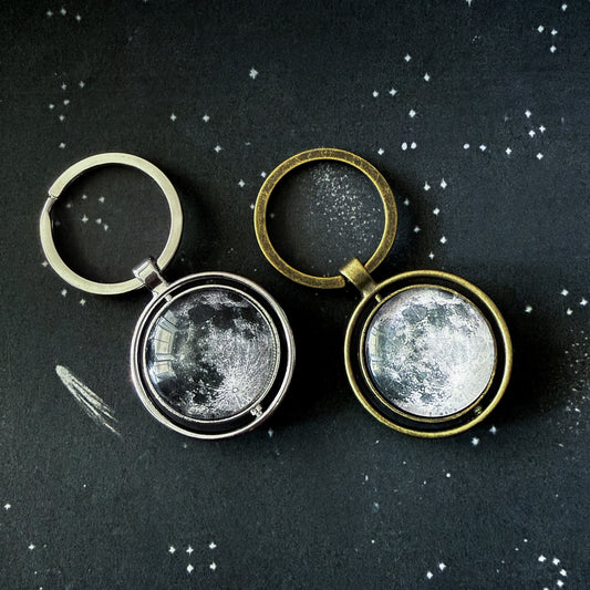 Two moon-themed keychains on a dark background with star-like dots.