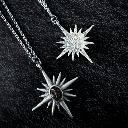 Two sun-shaped silver pendants on a chain against a dark background