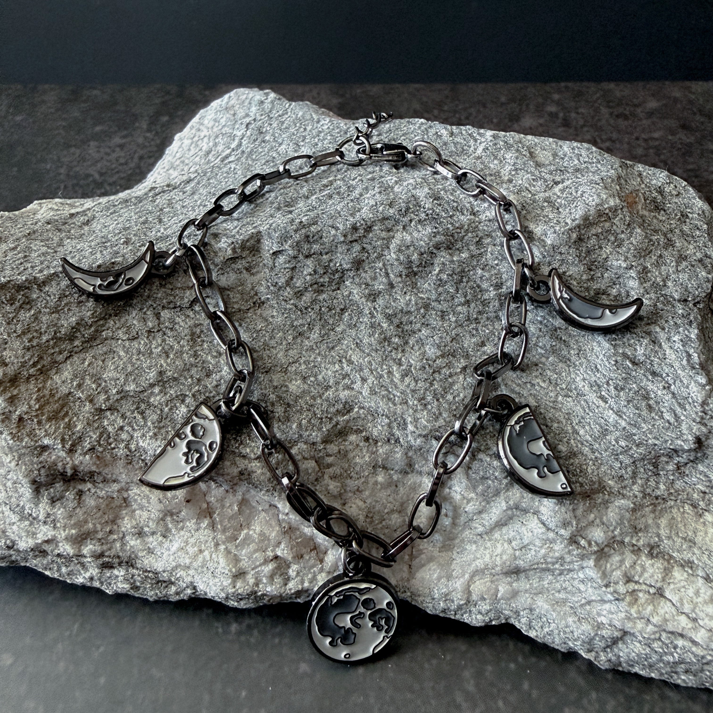 Silver bracelet with moon phase charms on a stone surface