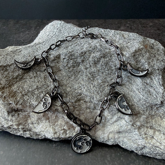 Silver bracelet with moon phase charms on a stone surface